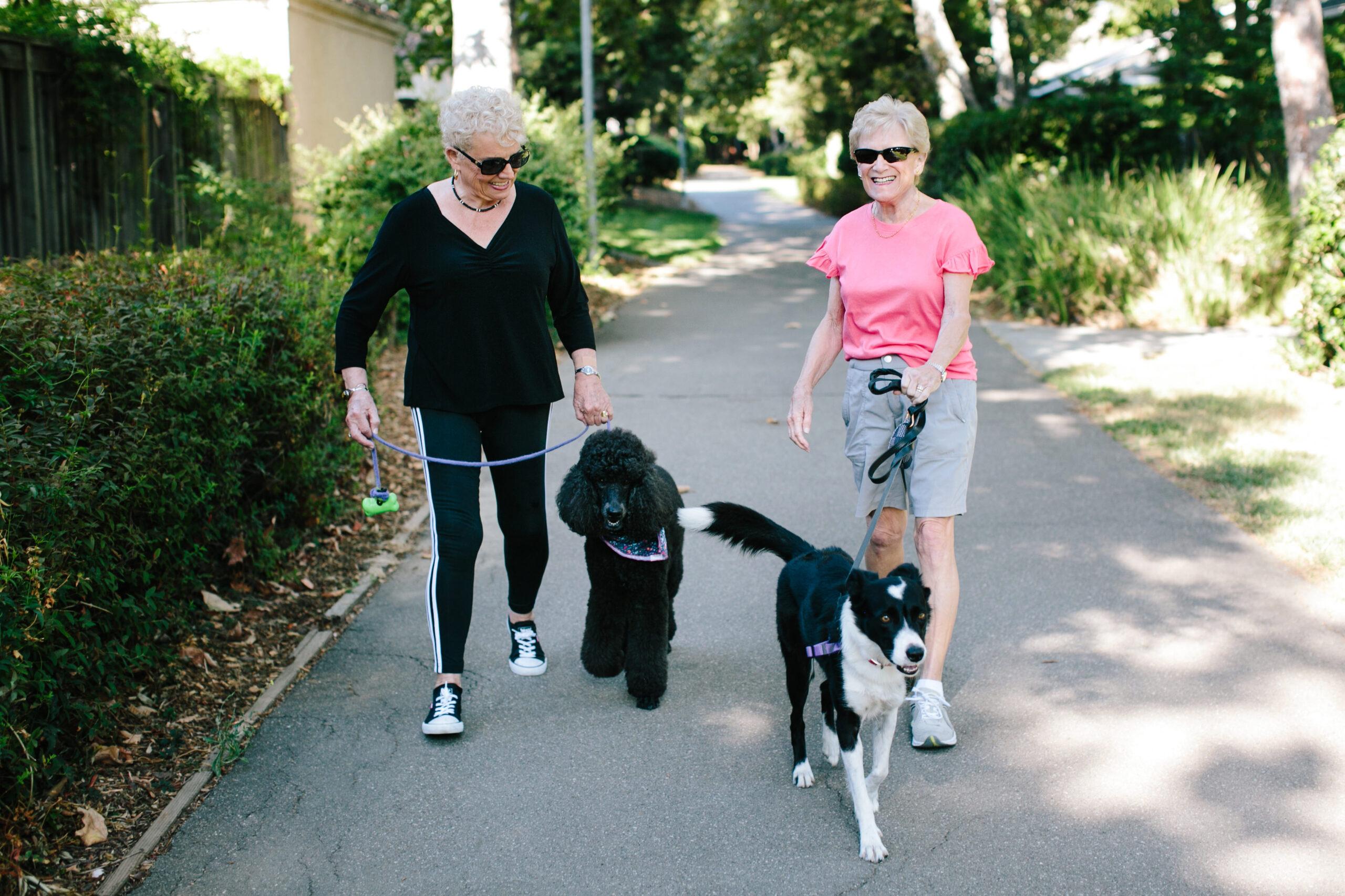 Two women walk dogs and smile