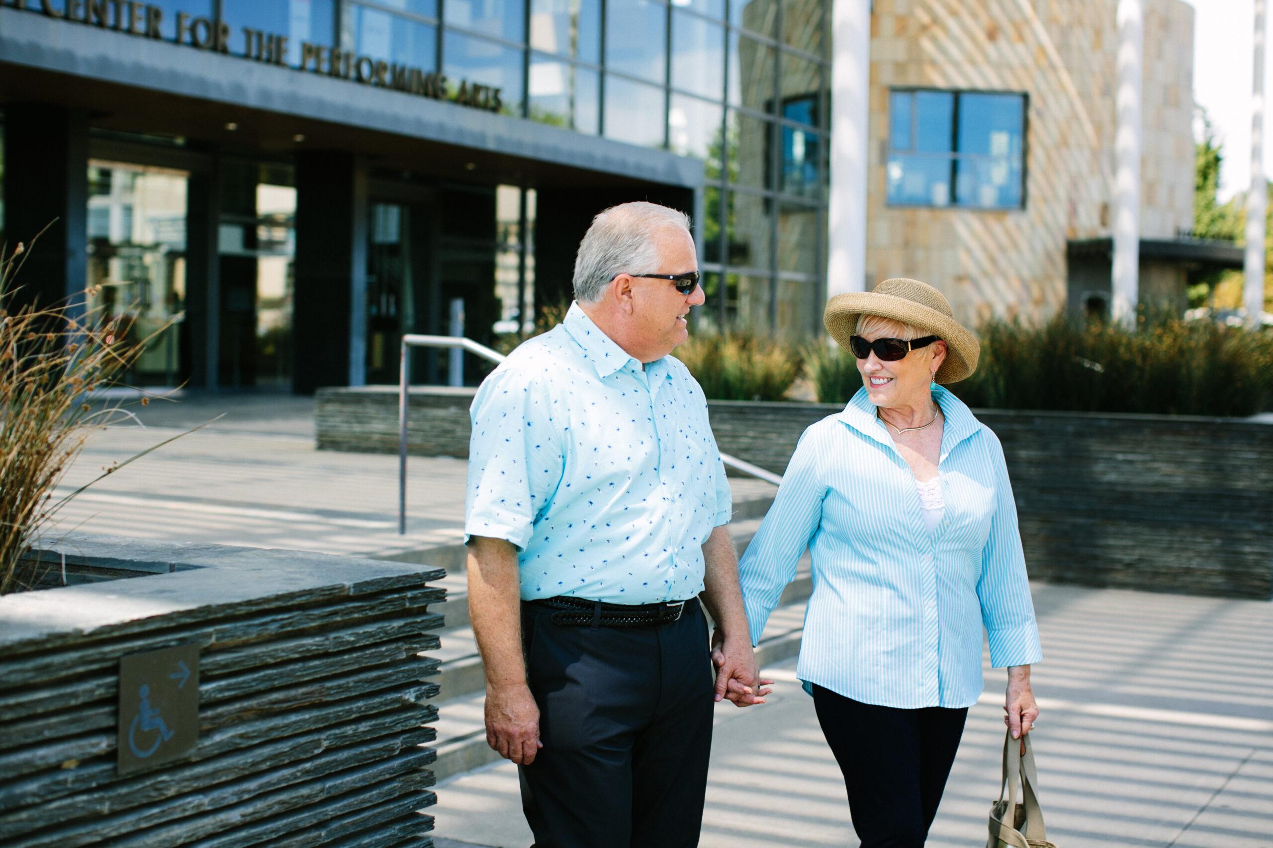 A stylish senior couple smiles and holds hands outdoors