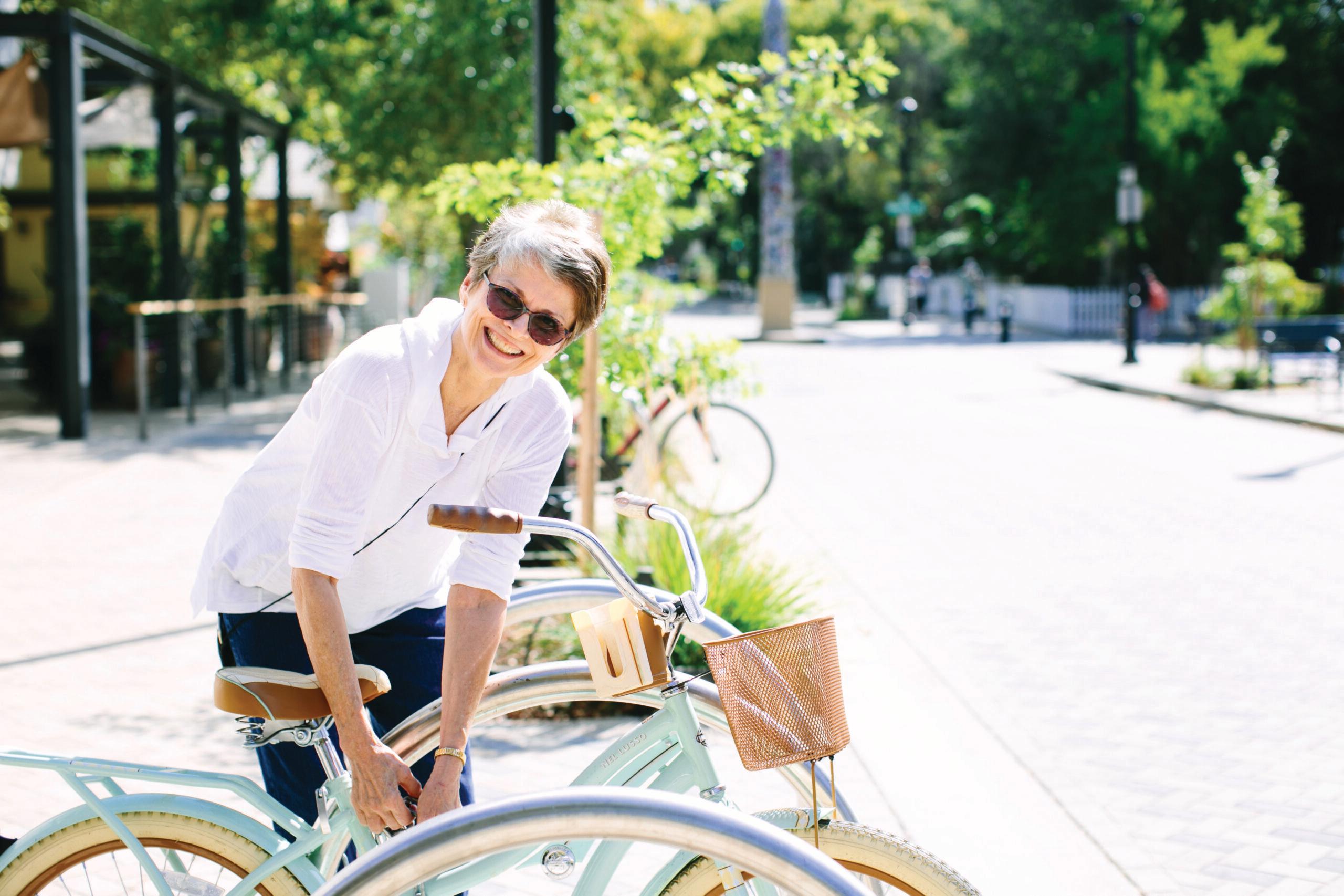 A woman wearing sunglasses smiles as she holds a bicycle