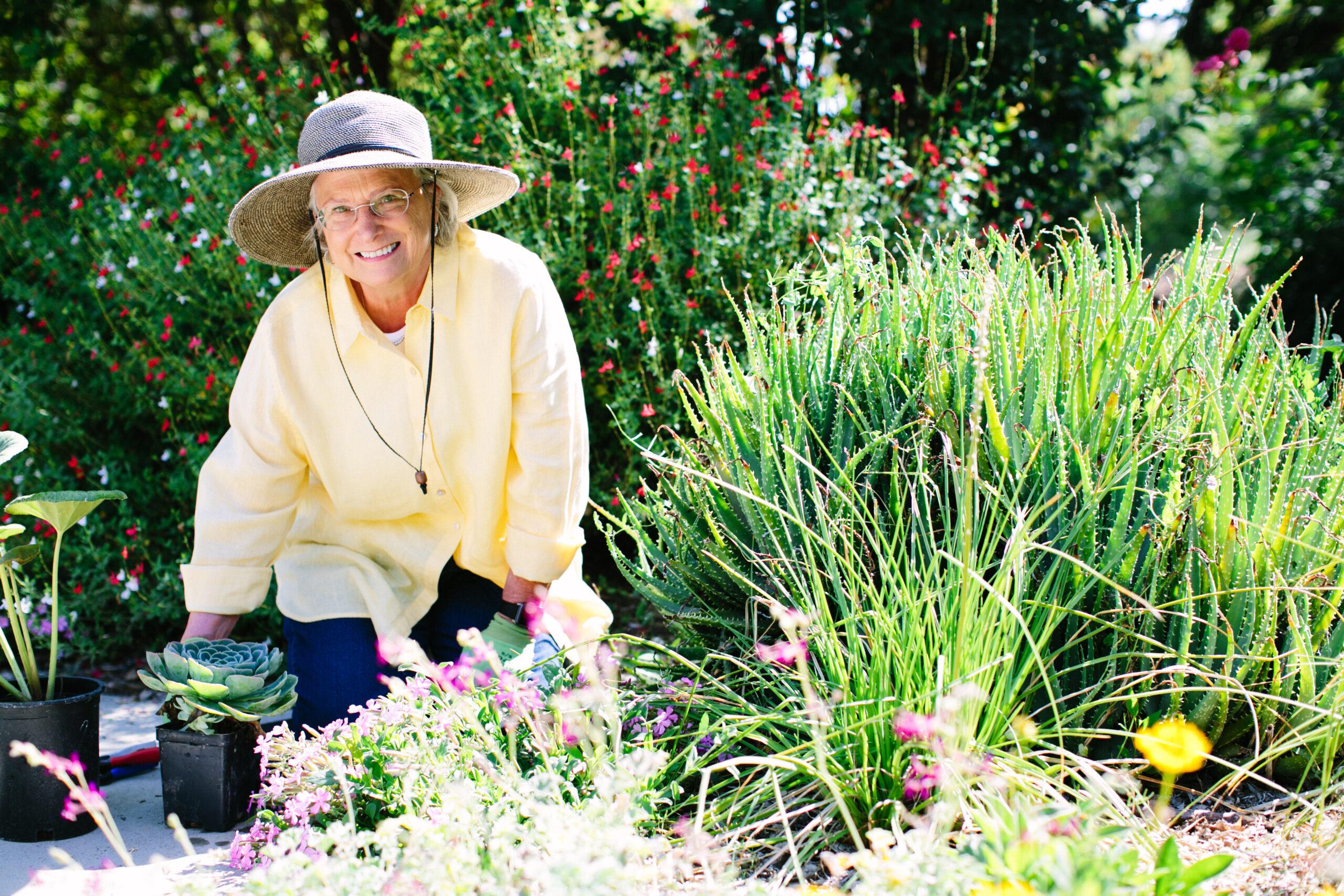 An older woman wearing a sun hat and yellow shirt is gardening