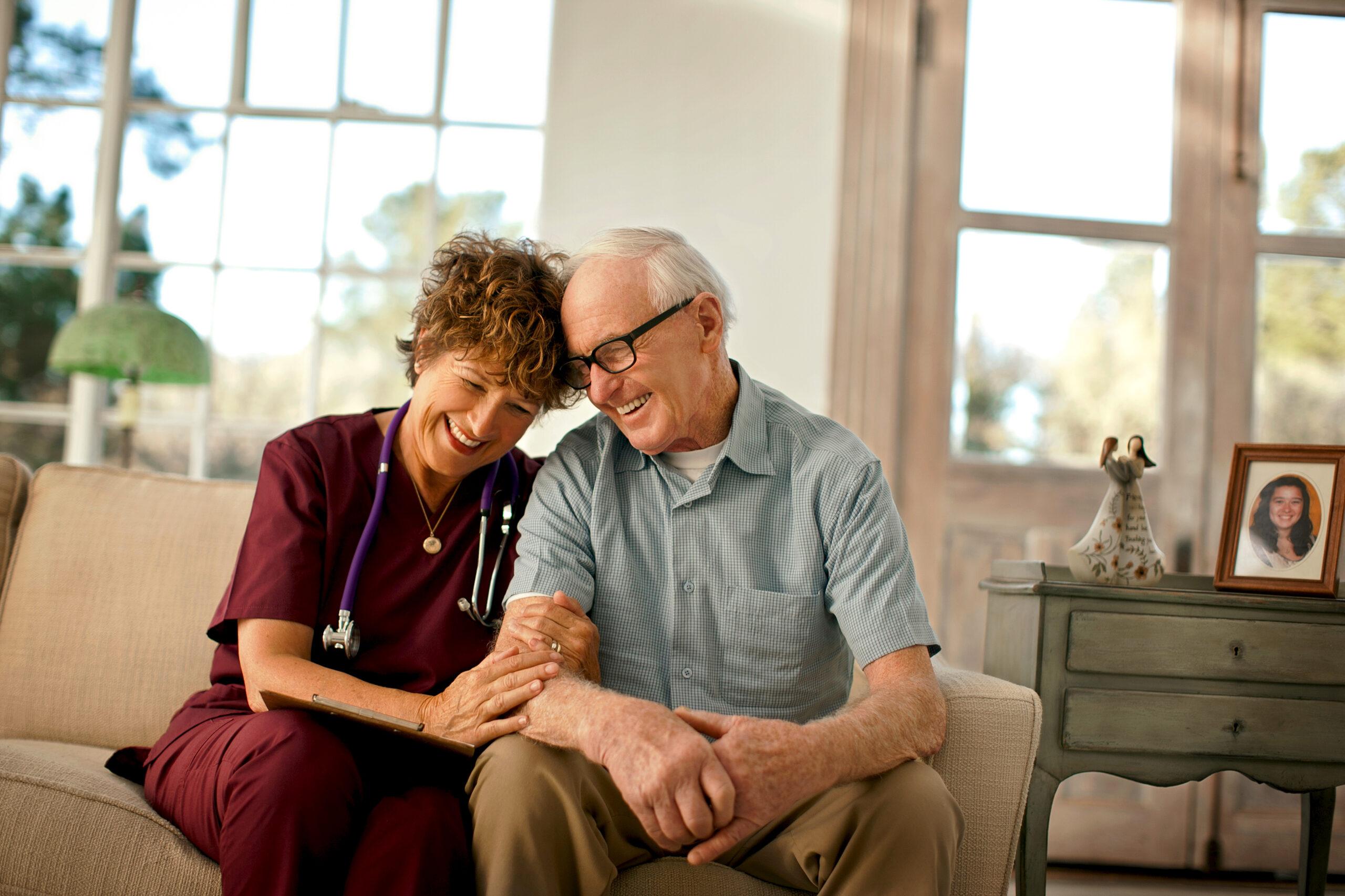 A smiling nurse comforts an older man during a home visit