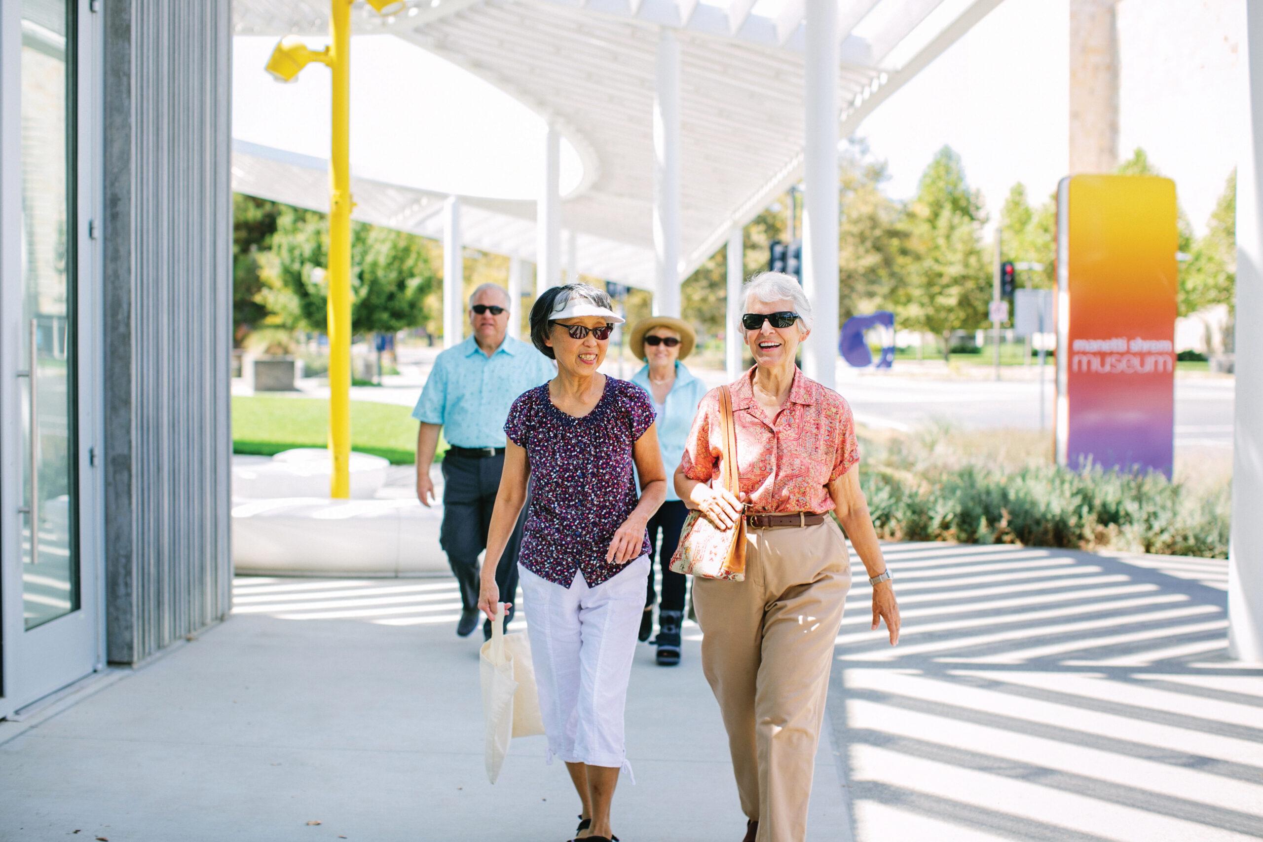 Older women wearing sunglasses walk in front of a museum