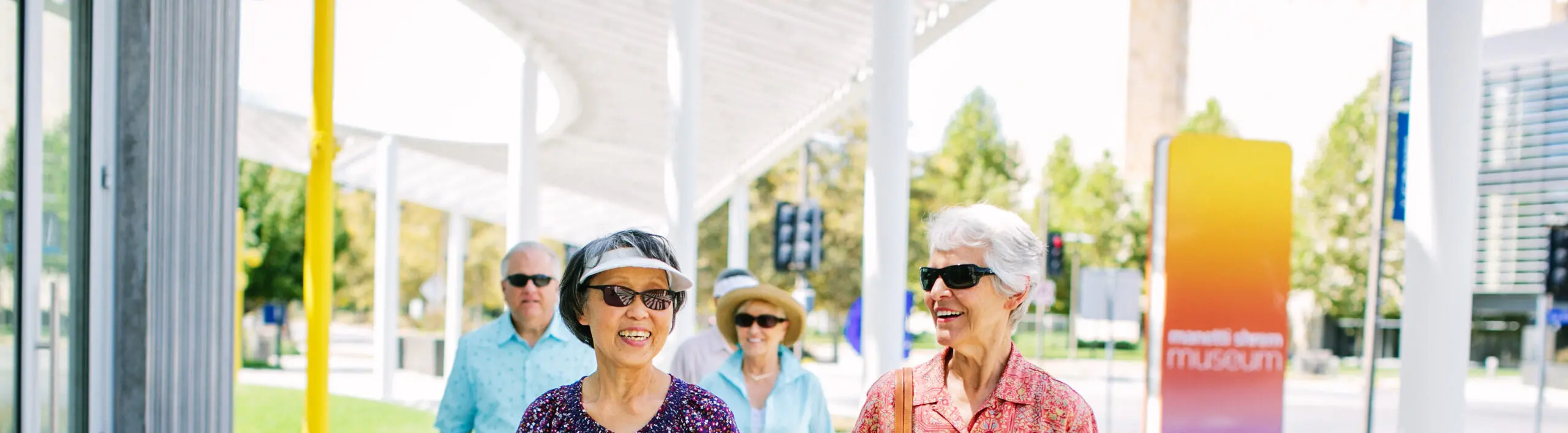 Smiling senior women wearing sunglasses walk in front of a museum