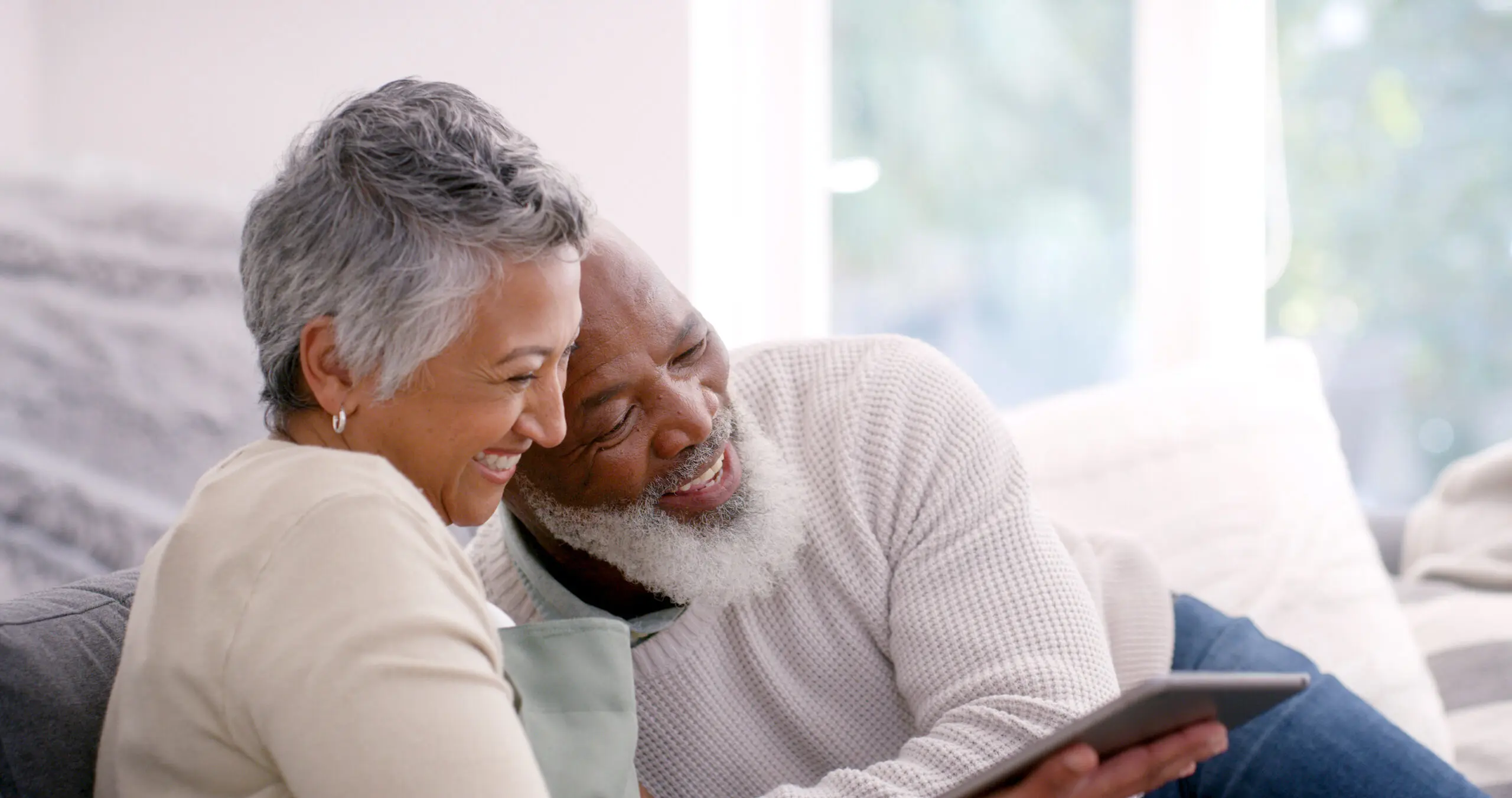 A happy couple browsing the internet on a tablet, cozy on the couch.